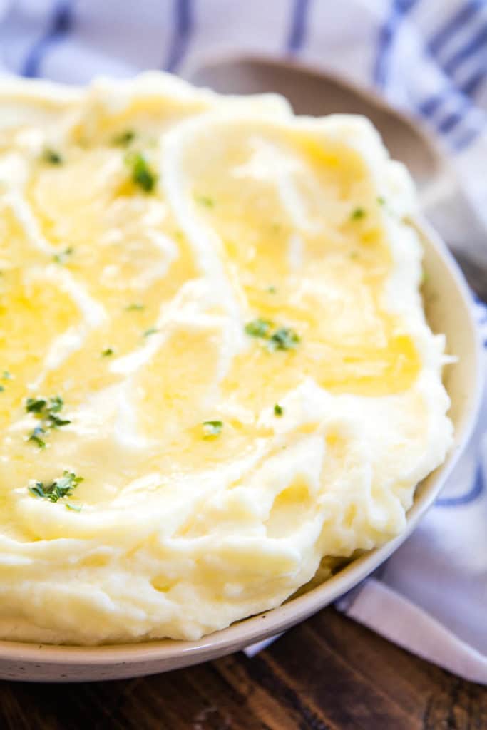 Picture showing half of a bowl of mashed potatoes butter melted on top and garnish with parsley