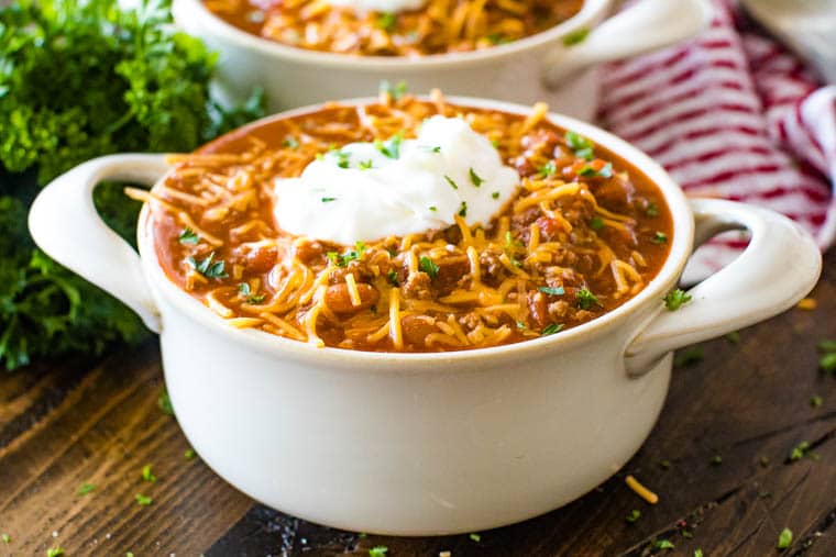 Ceramic bowl of chili topped with shredded cheddar cheese, sour cream and minced parsley.