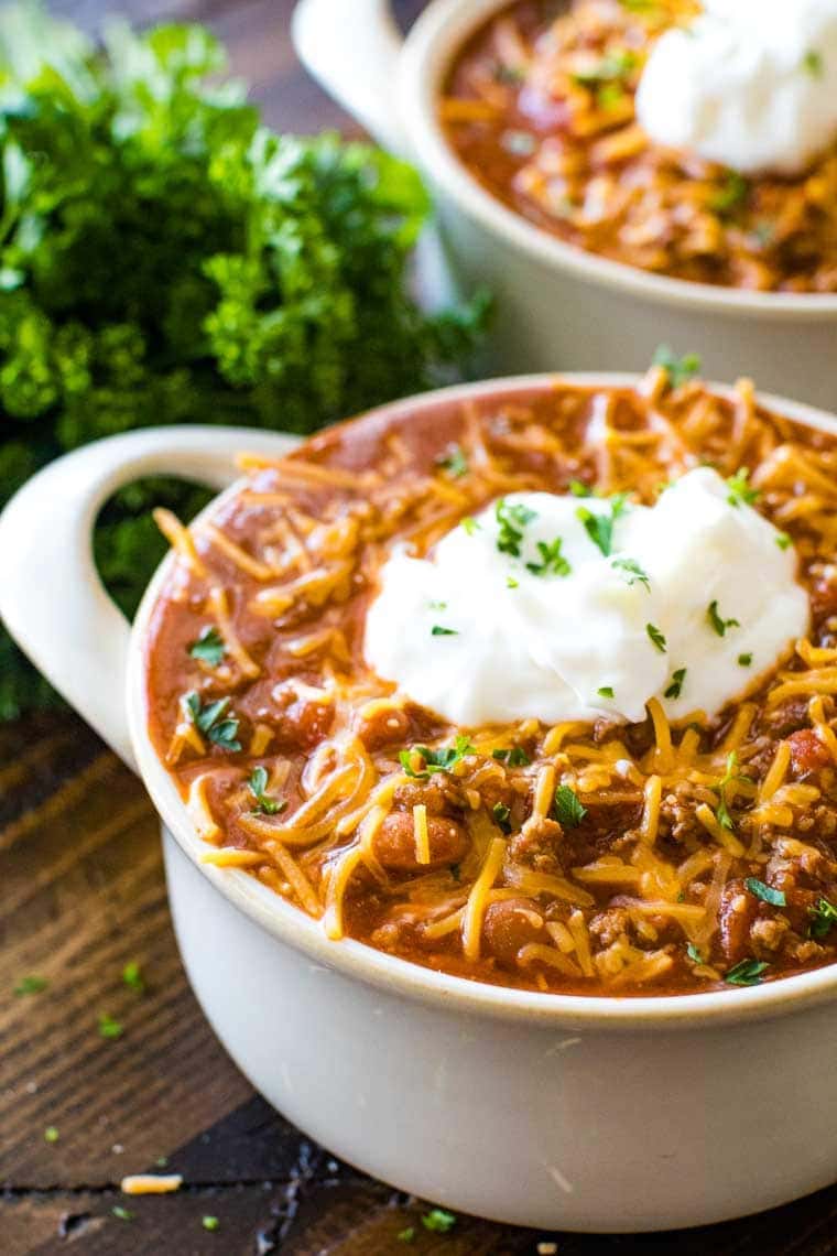 Clay soup bowl with chili in it topped with shredded cheddar cheese and a dollop of sour cream