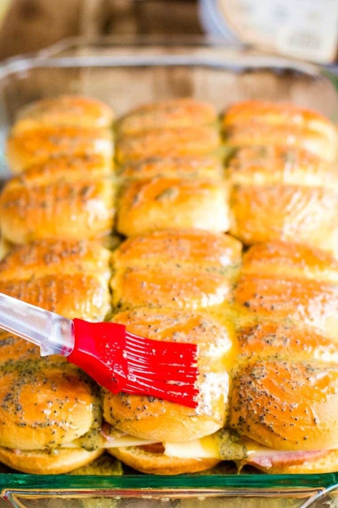 Silicone brush putting on buttery topping on a pan of sliders