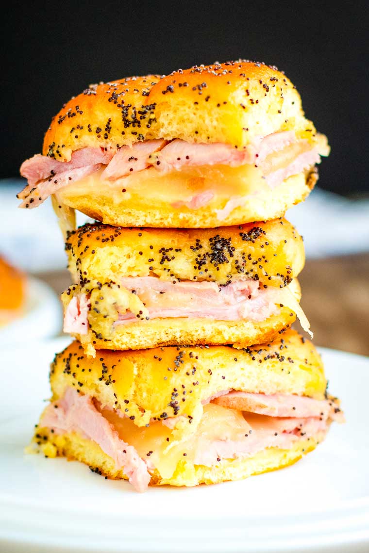 Vertical stack of three ham and cheese sliders on white plate