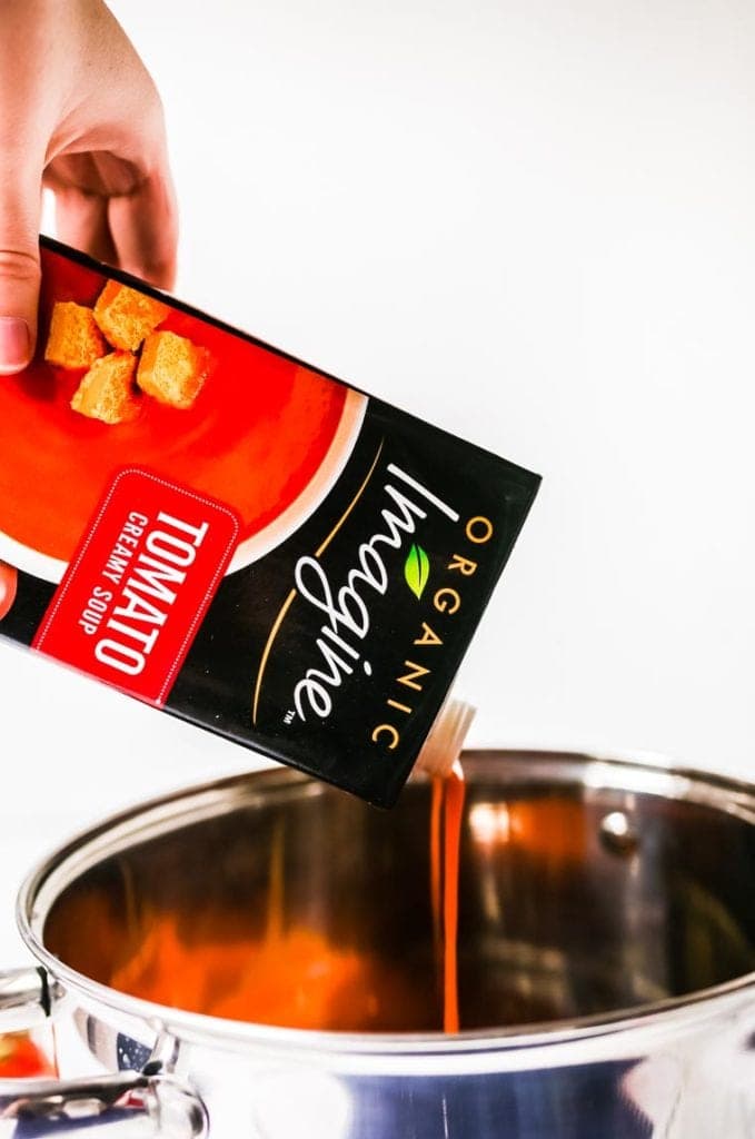 Hand pouring Imagine Tomato soup into pot