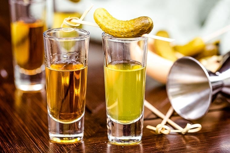 A shot of whiskey and a shot of pickle juice brine garnished with a pickle