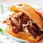 Hand holding a pulled pork sandwich with bbq sauce