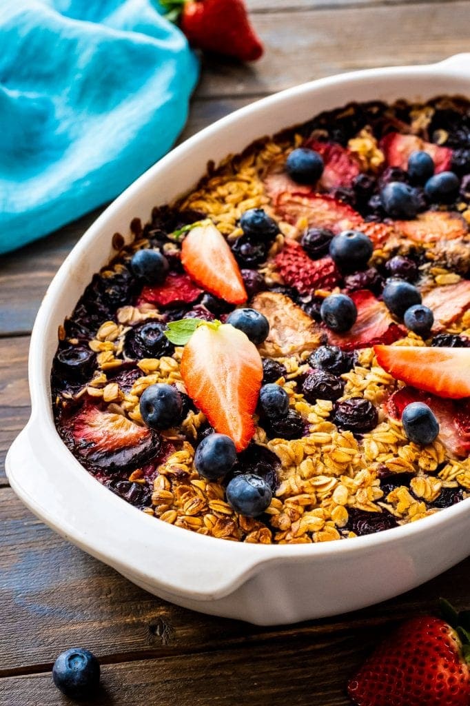 White Baking Dish with Baked Oatmeal topped with strawberries and blueberries on dark wooden background