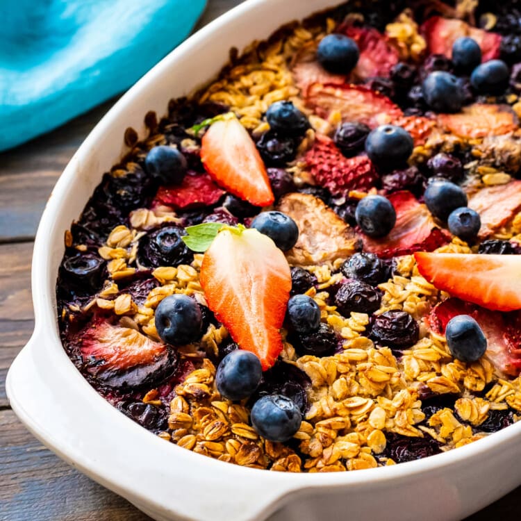 White Baking Dish with Baked Oatmeal topped with strawberries and blueberries on dark wooden background