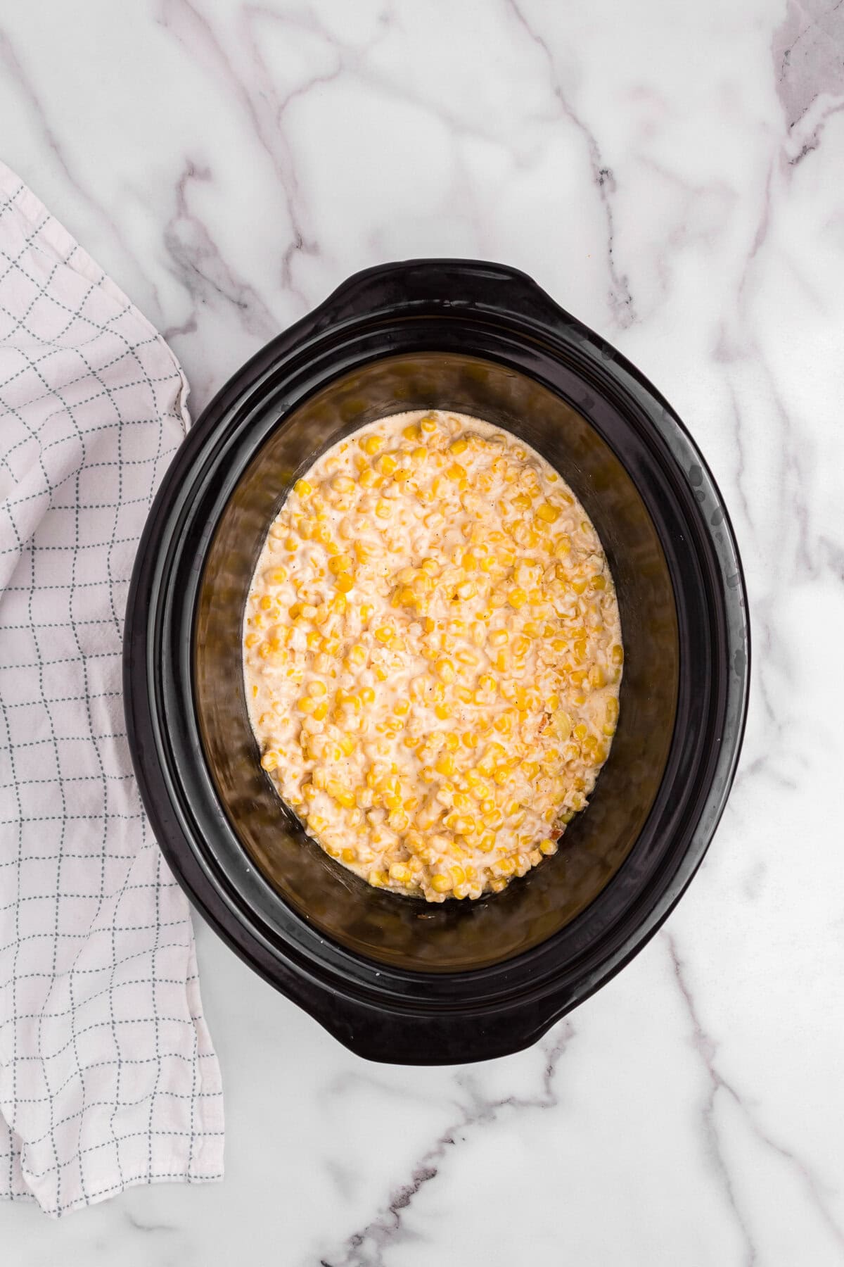 Creamed corn mixture smoothed out in the slow cooker after being mixed and heated, beginning to meld into a creamy consistency.