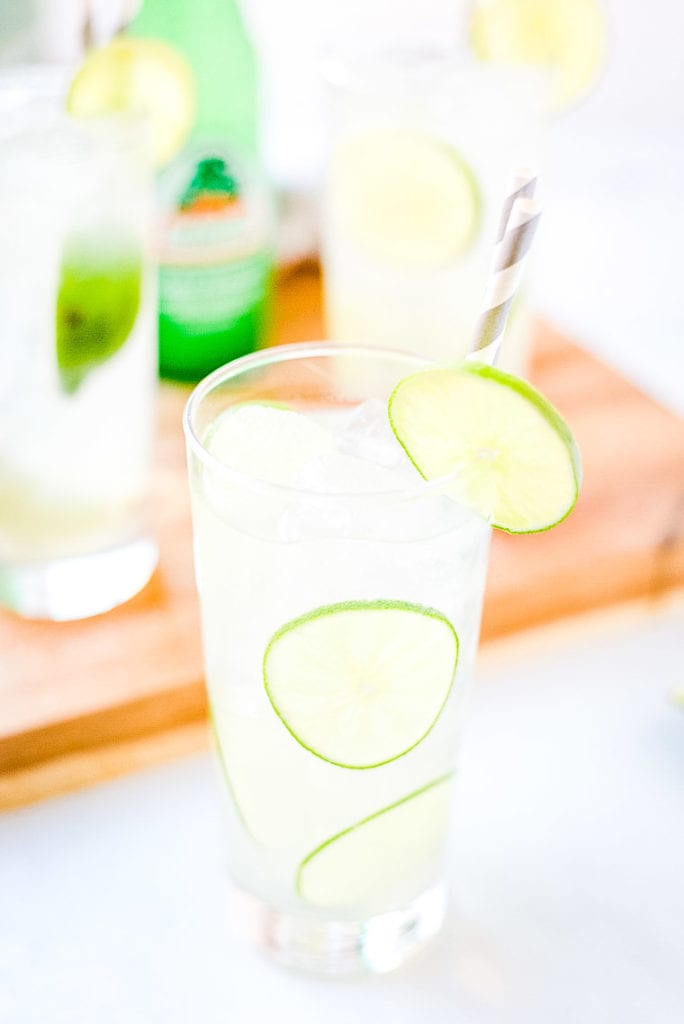 Paloma in glass with lime slices in cocktail and garnishing rim. A gray and white striped paper straw in drink.