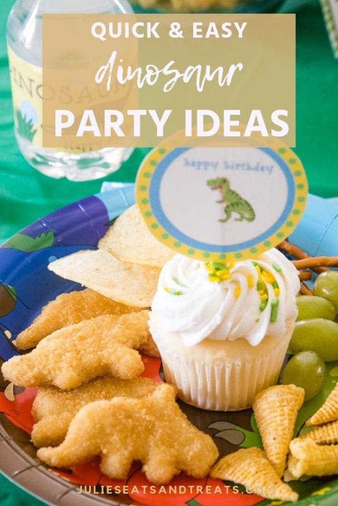 Dinosaur happy birthday sign in a vanilla cupcake on a plate with dino chicken nuggets, potato chips, bugels, and grapes