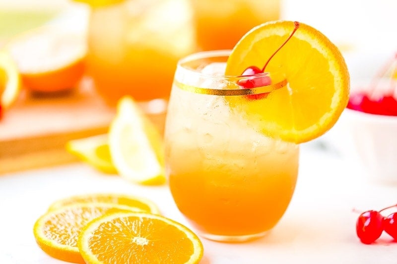 Drink in glass with garnishes and orange slices and cherries laying next to it