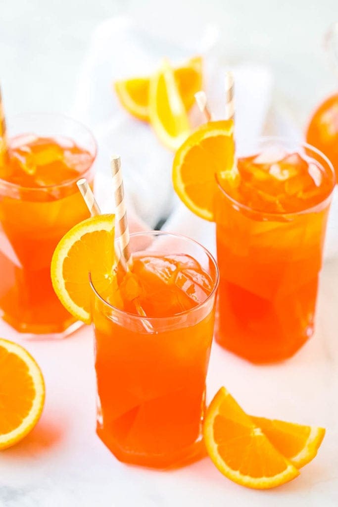 Marble background with Cocktail glasses full of Aperol Spritz garnished with a slice of orange and gray and white paper straws