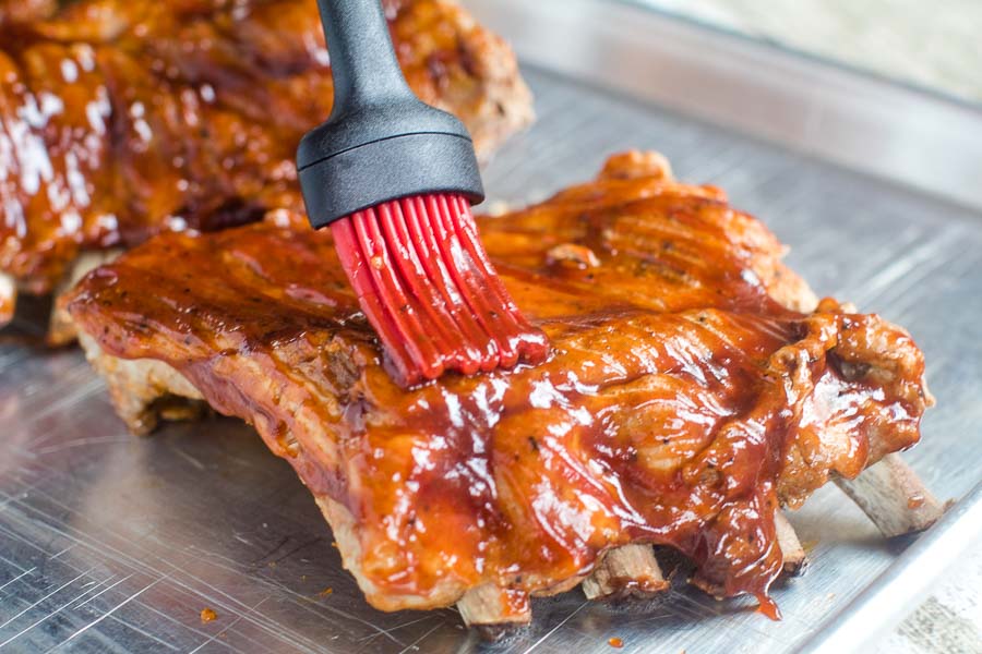 Basting brush putting on bbq sauce on baby back ribs