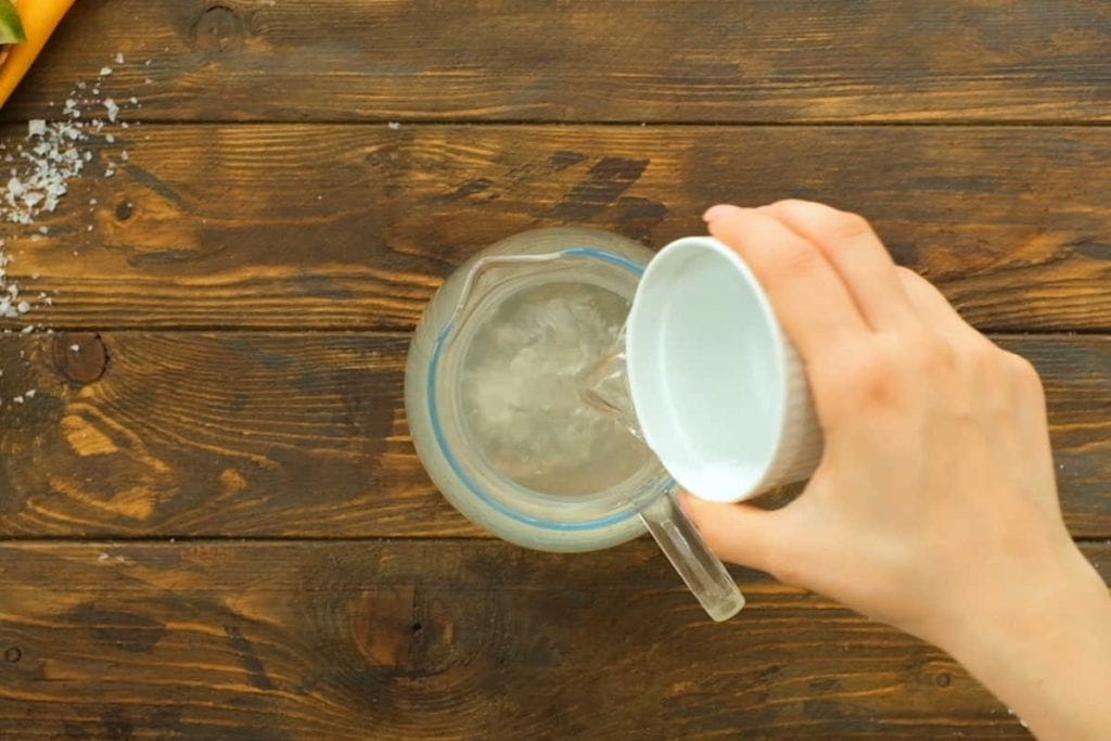 Pouring a white bowl of alcohol into glass pitcher.