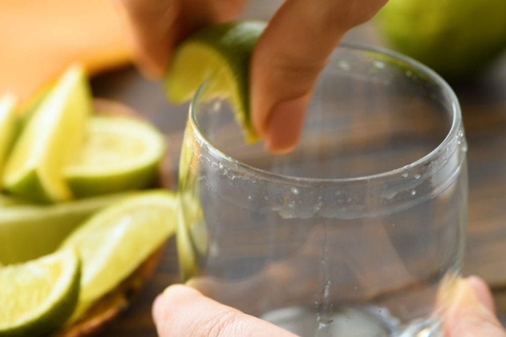 Two hands rimming glass with lime wedge