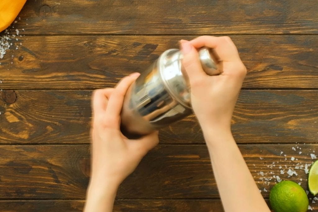 Two hands shaking a shaker for margaritas