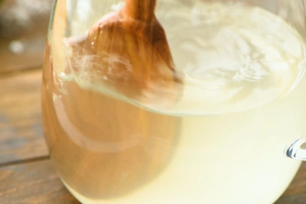 Stirring ingredients for margaritas with wooden spoon in a glass pitcher.