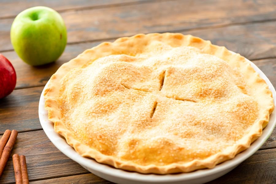 Freshly baked apple pie in white baking dish with four slits that's topped with a sugar. 