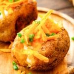 Baked Potatoes topped with shredded cheese on cutting board