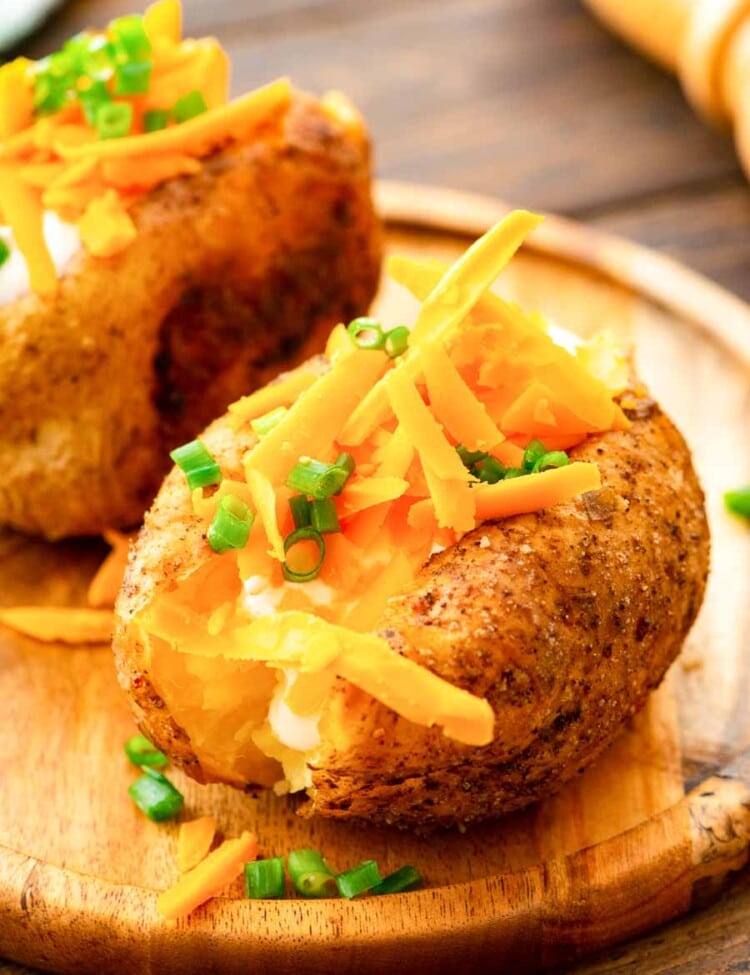 Baked Potatoes topped with shredded cheese on cutting board