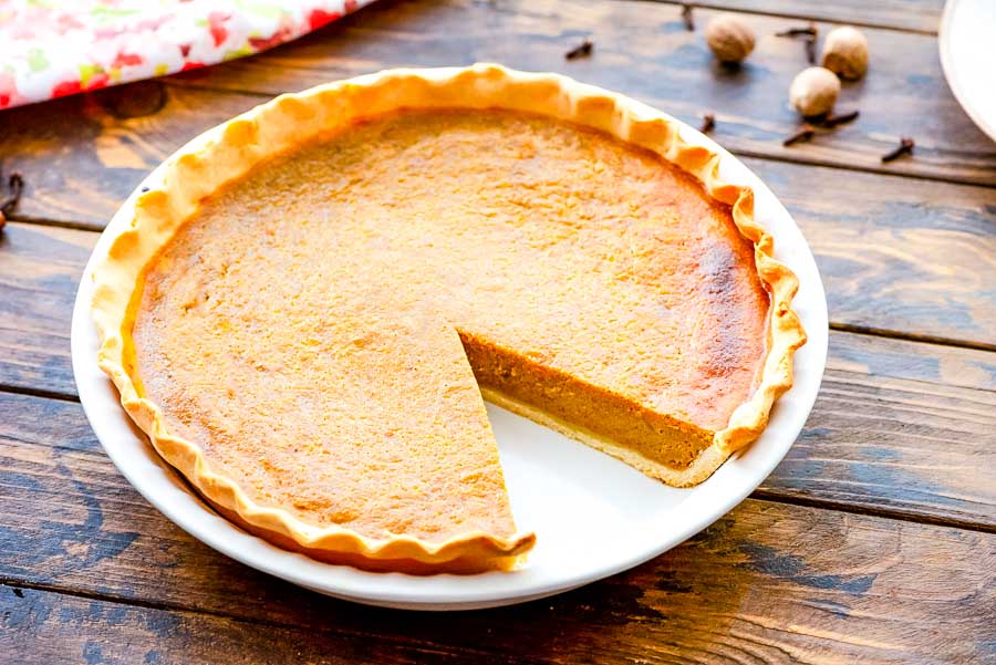 Pumpkin Pie in white pie plate with a slice taken out of it.