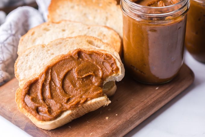 Toast smeared with pumpkin butter and a bite taken out of it sitting on wood cutting board with a jar of pumpkin butter next to it.