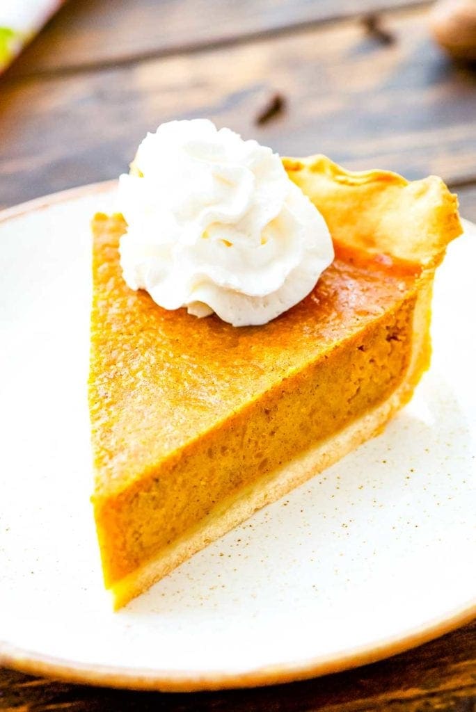 Pumpkin Pie slice on white plate with a dallop of whipped cream on top.