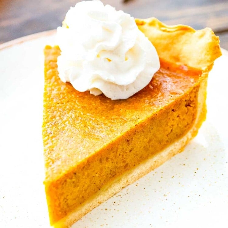 Pumpkin Pie slice topped with whipped cream on a white plate