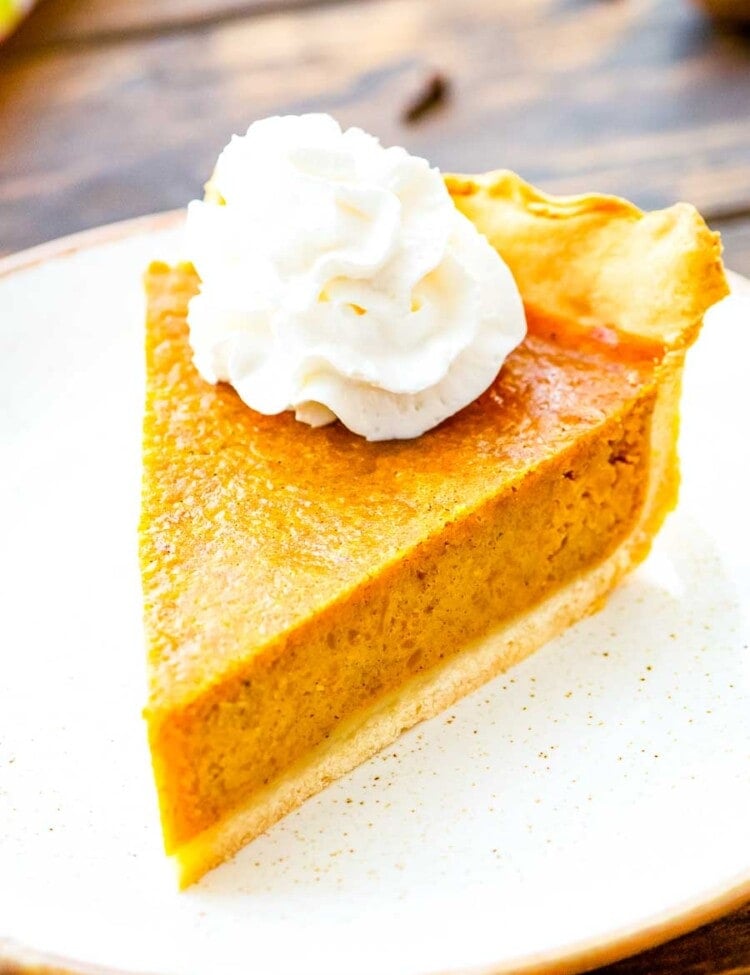 Pumpkin Pie slice topped with whipped cream on a white plate