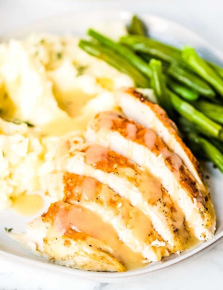 Slices of turkey, mashed potatoes, green beans, and gravy on a plate