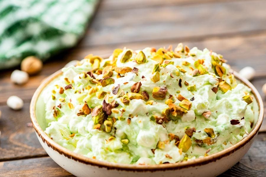 Pottery bowl of watergate salad topped with chopped pistachios on a wooden background