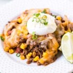 white plate with taco casserole on it topped with sour cream