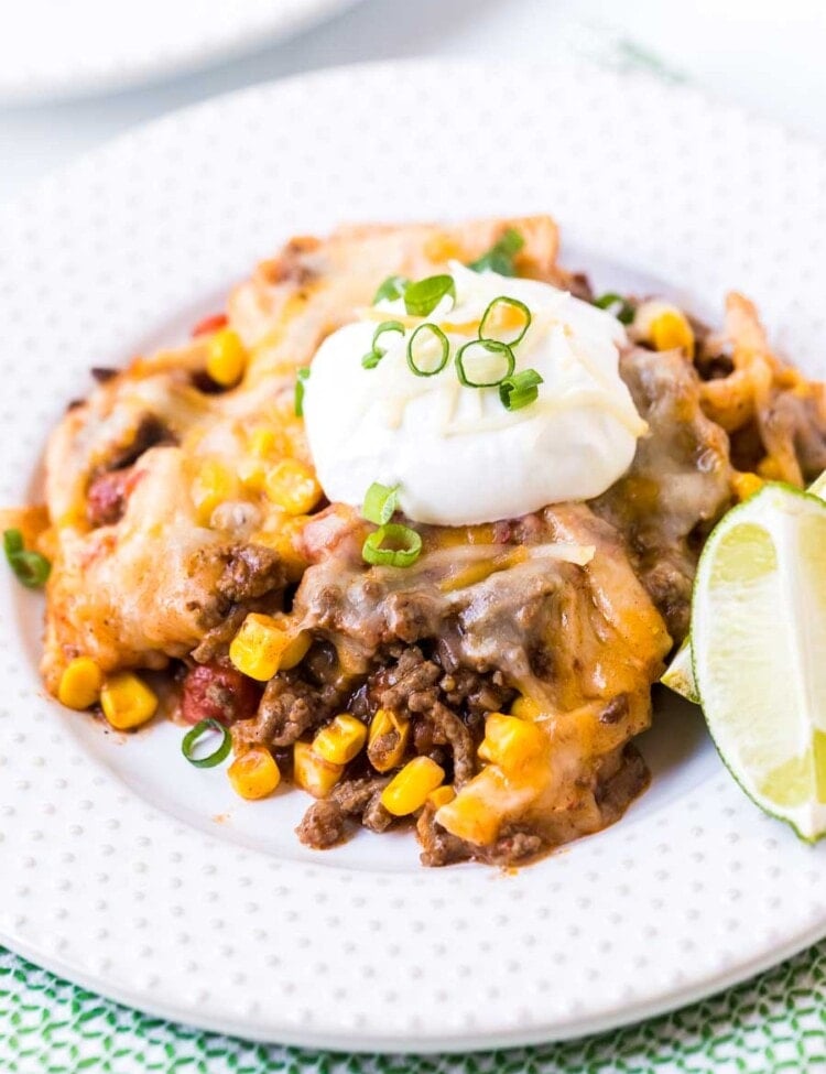 white plate with taco casserole on it topped with sour cream