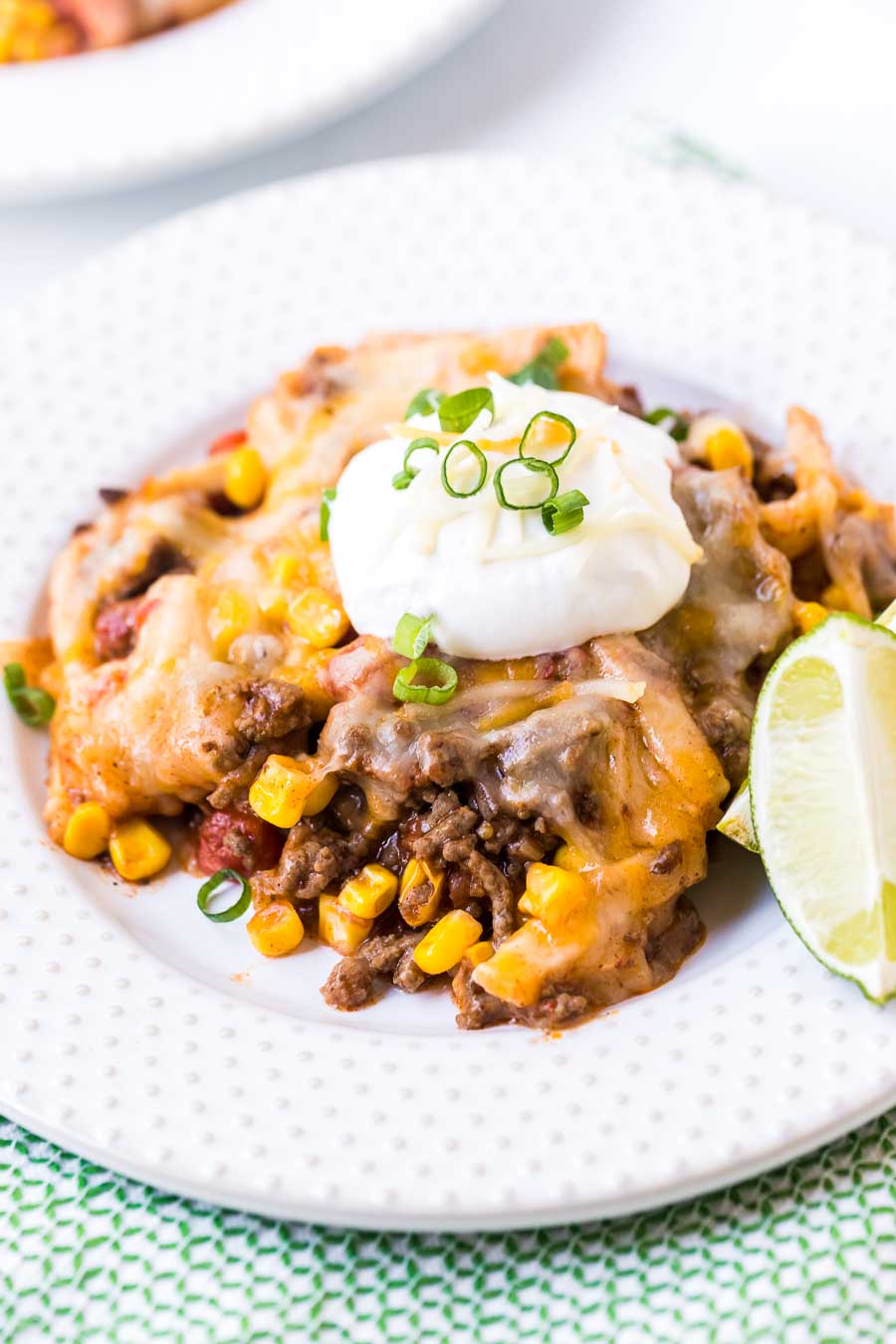 White plate with taco casserole topped with sour cream, green onions and cheese