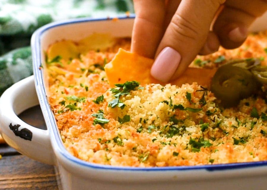 Hand dipping a chip into a dish of jalapeno popper dip