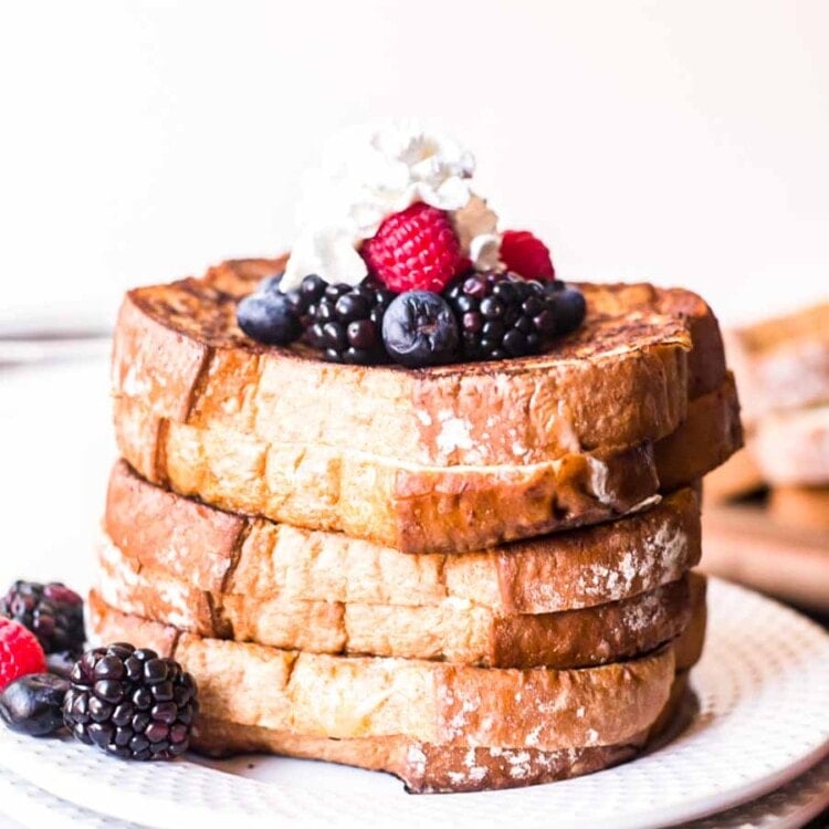 Stack of stuffed french toast topped with whipped cream and berries on a plate