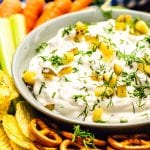 bowl with dill pickle dip surrounded by pretzels, chips, celery, and carrots