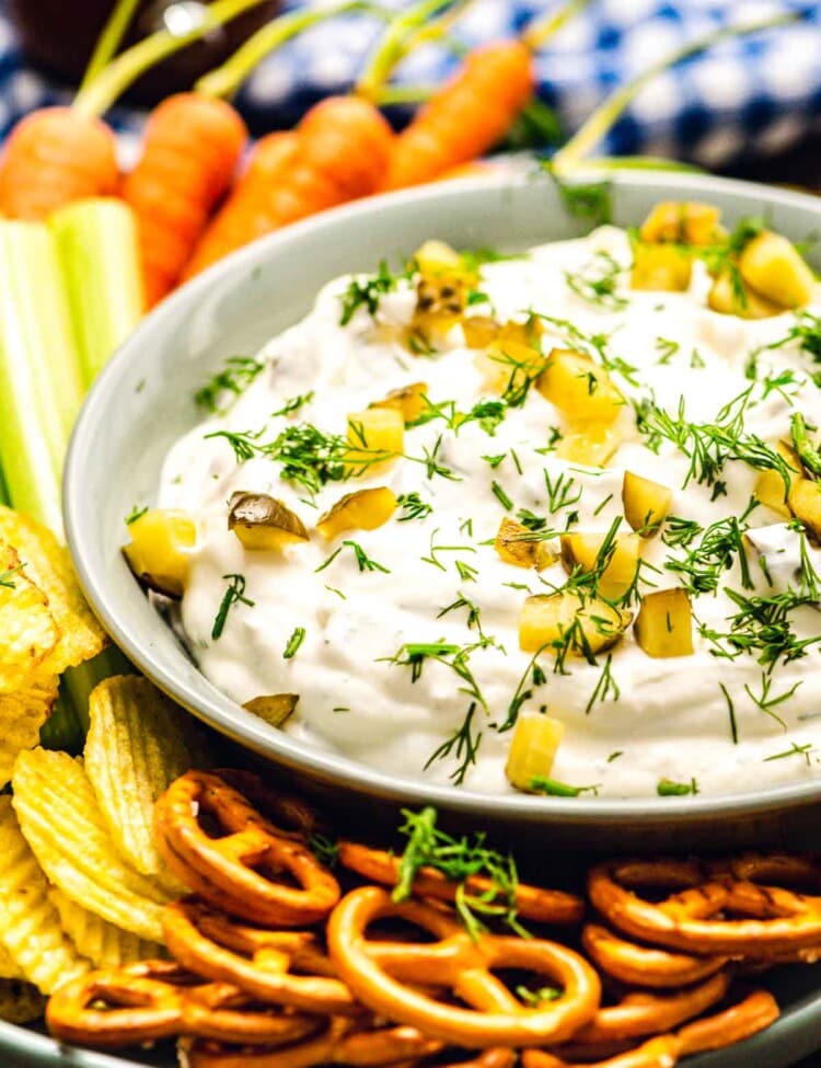 bowl with dill pickle dip surrounded by pretzels, chips, celery, and carrots