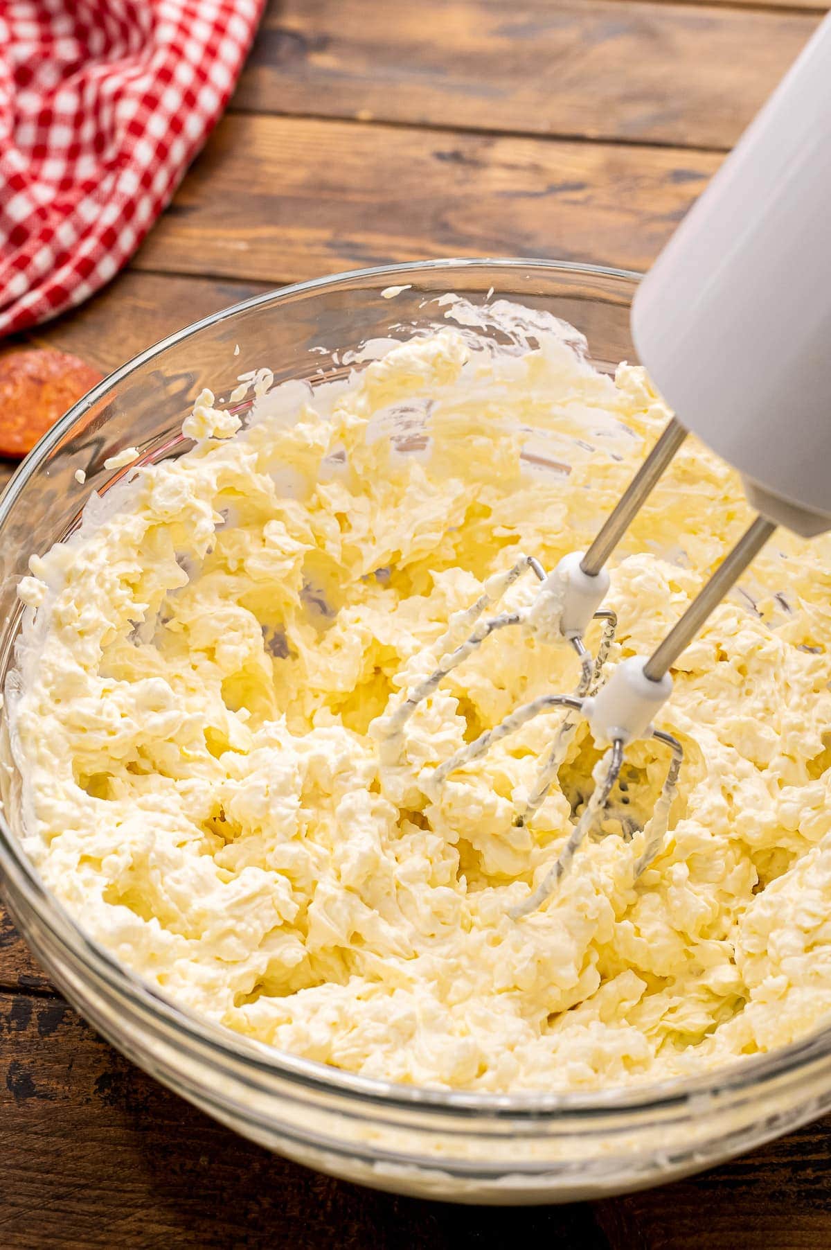 Hand mixer combining pizza dip ingredients in glass bowl.