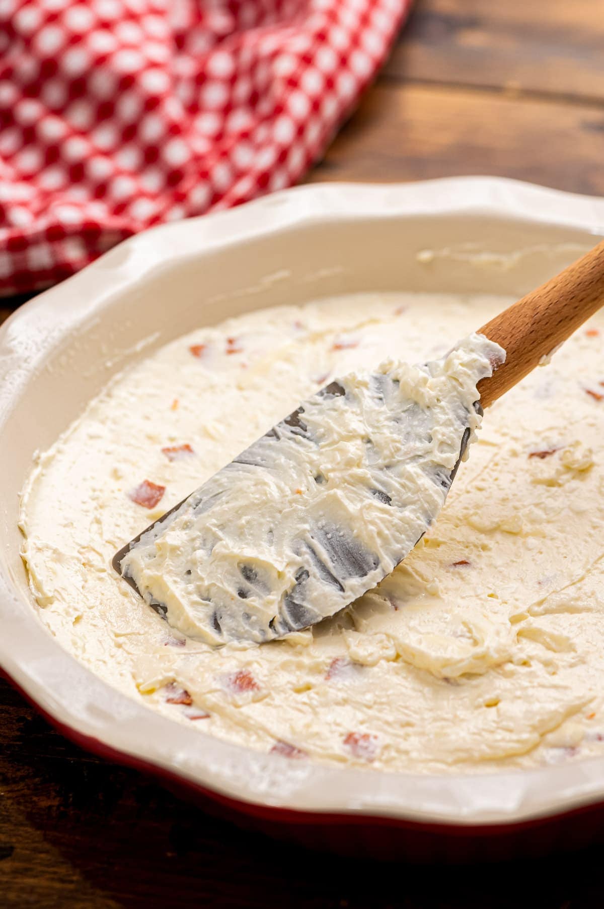 Spatula spreading out pizza dip in a pie plate.