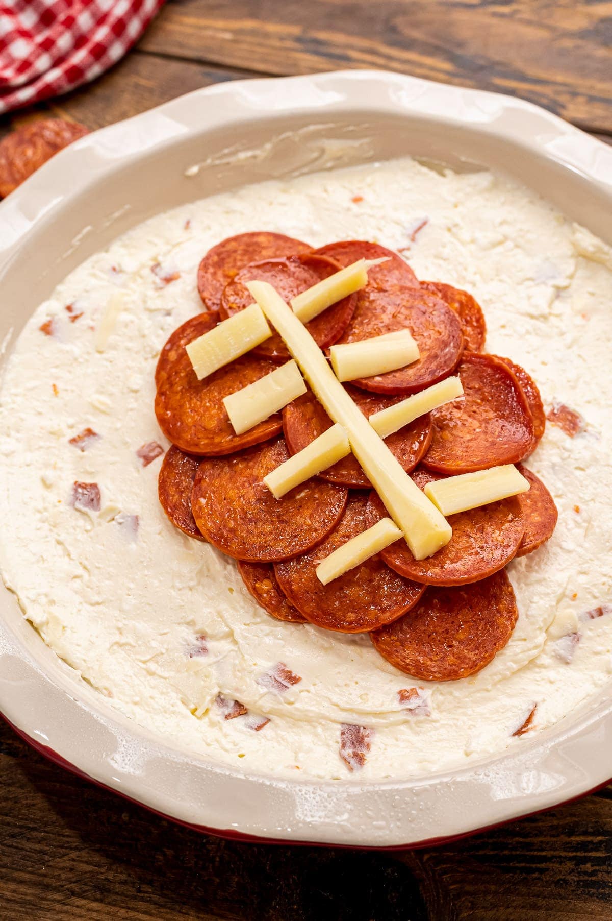 Overhead image of football pepperoni pizza dip in pie plate before baking.