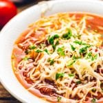 White bowl of lasagna soup topped with shredded cheese.