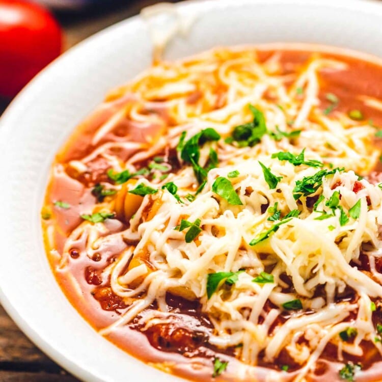 White bowl of lasagna soup topped with shredded cheese.