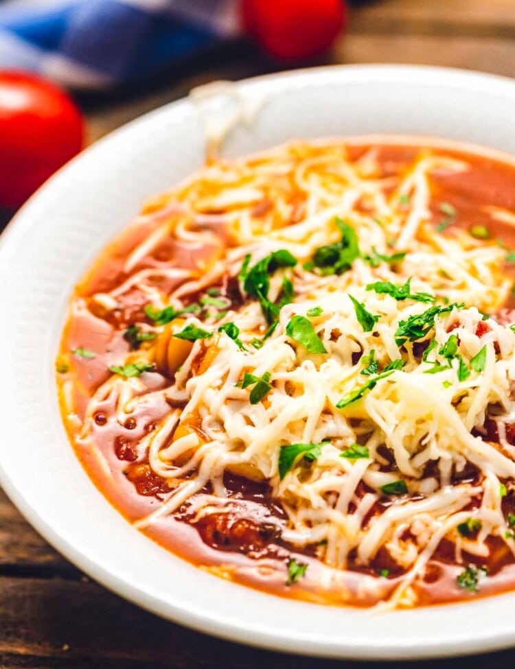 White bowl of lasagna soup topped with shredded cheese.