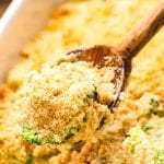 Wooden spoon scooping broccoli casserole out of a white baking dish