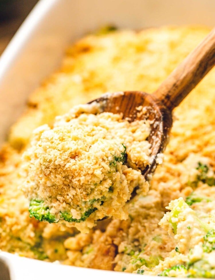 Wooden spoon scooping broccoli casserole out of a white baking dish