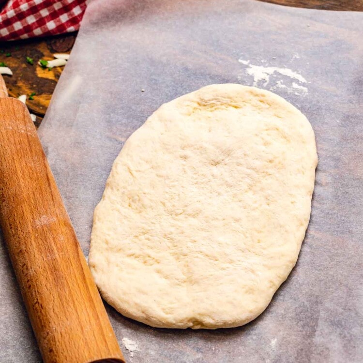 pizza dough on wax paper with a rolling pin