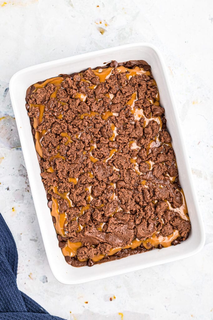 Overhead image of spoonfuls of brownie batter dropped on top of caramel for brownies.