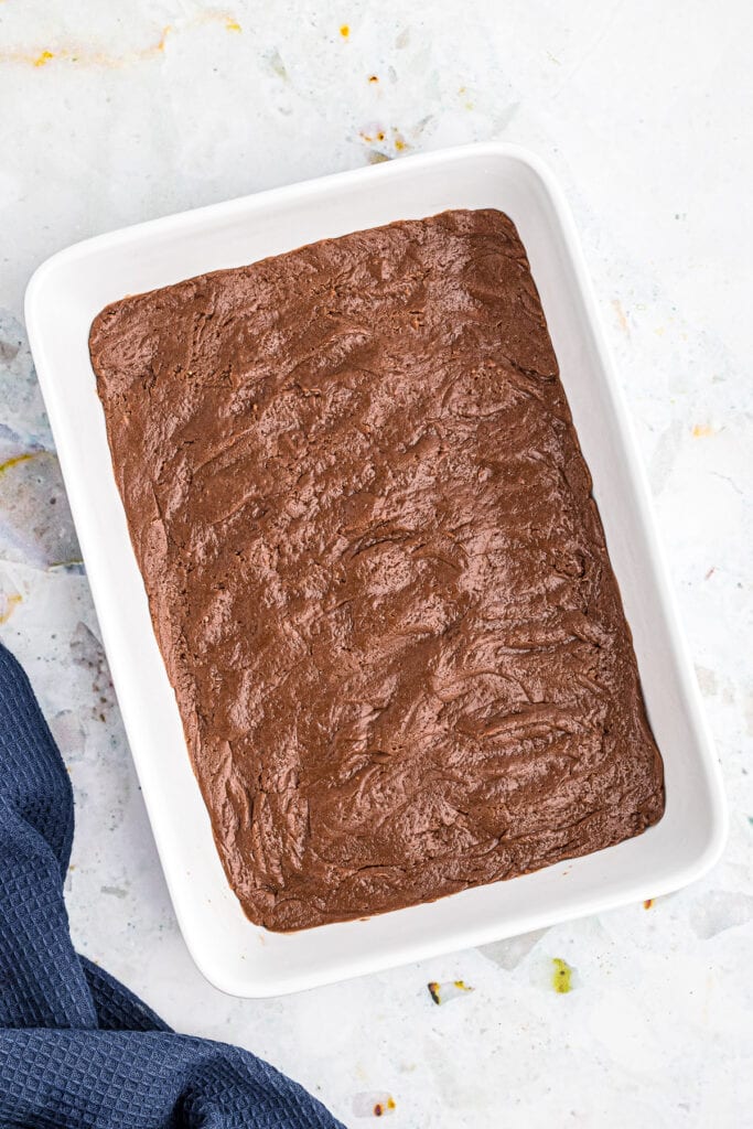 Overhead image of white baking dish with a thin layer of chocolate brownie mix on bottom before baking