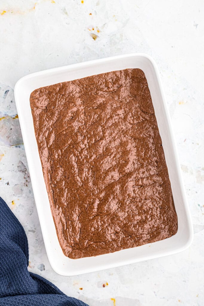 Overhead image of white baking dish with a thin layer of chocolate brownie mix on bottom after baking