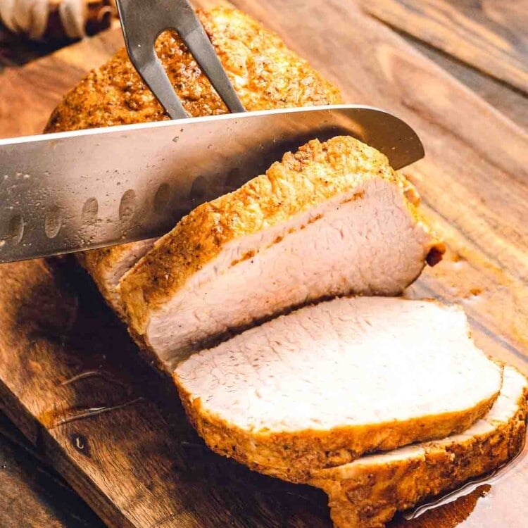 Pork loin being sliced on a wood cutting board